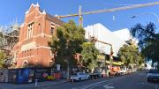 Behind a heritage building sits a white box style new building, a large crane is overhead.